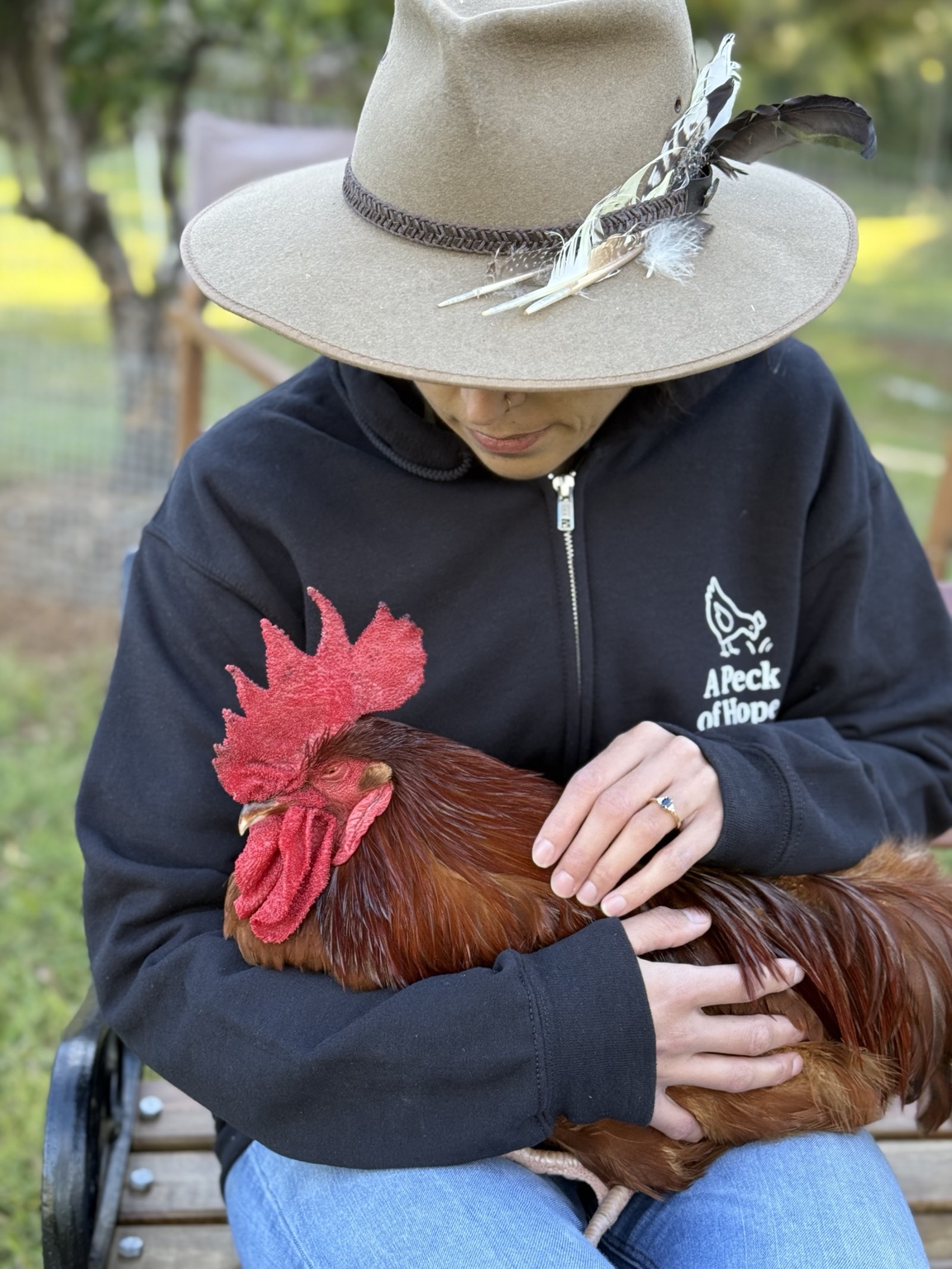 Eddie resting in a carer’s arms outdoors, with the A Peck of Hope logo on their jumper